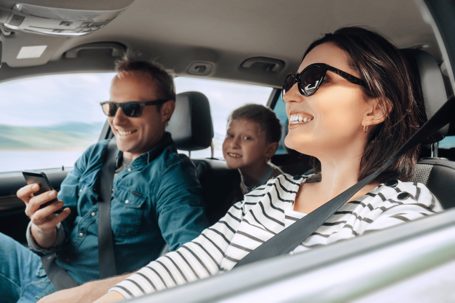 Smaidīgi tētis, mamma un dēls ceļo ar elektroauto.