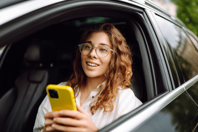 Smaidoša meitene elektroauto savā tālrunī izmanto Ignitis ON izveidotu maršrutu pa Vidzemi.